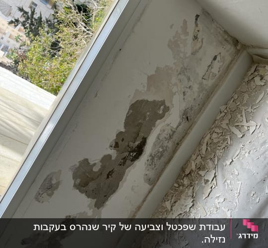 קיר מתקלף עם סימני רטיבות ליד חלון